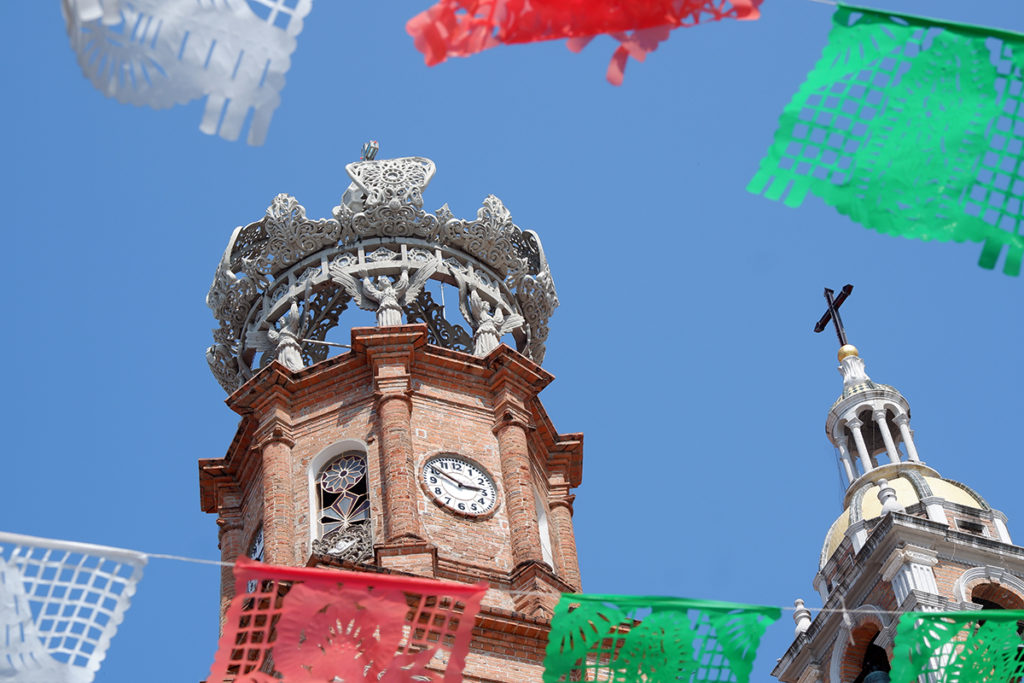 A quick guide to Downtown Puerto Vallarta: colourful decoration hung up across the street and a clock tower seen through them