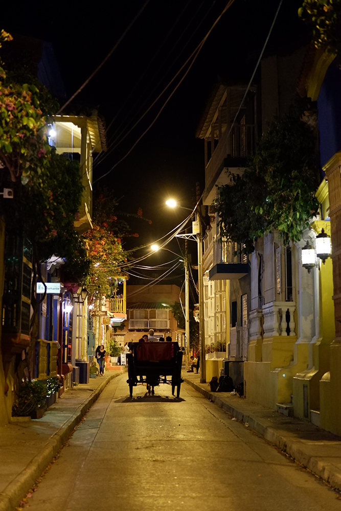 What to do and see Cartagena's Walled City and other Colombian basics: a dark street with a horse carriage traveling between the buildings 