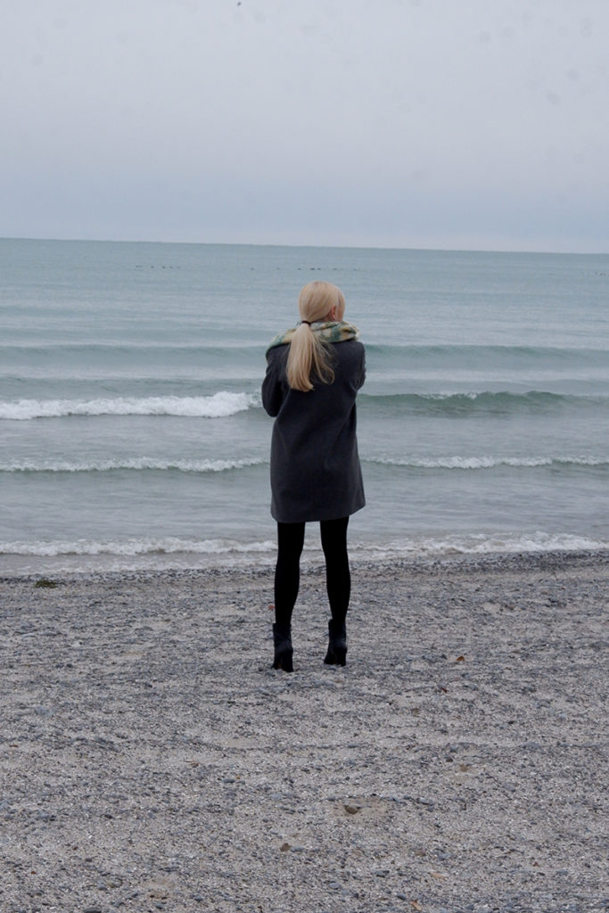 a woman standing on the beach in a warm coat 