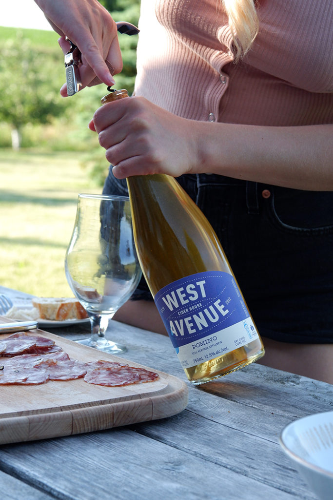 Experience the charm of West Avenue Cider cottage near Hamilton: a woman opening a cider bottle