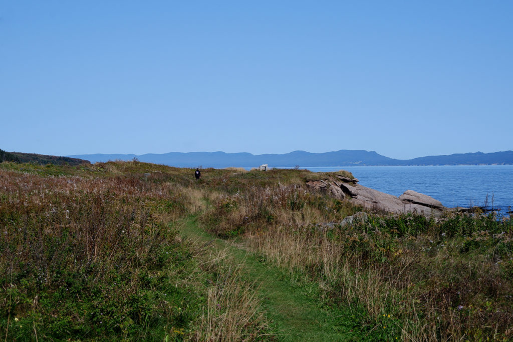 Destination guide: The great adventure through Quebec Maritimes, blue water and green field with mountains in the background 