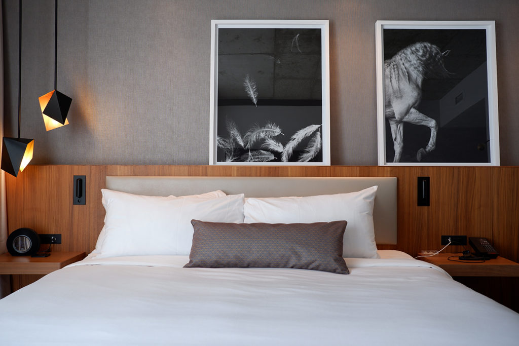 Montréal City Guide: Humaniti Hotel King bed framed by a backboard with two black and white prints of horses