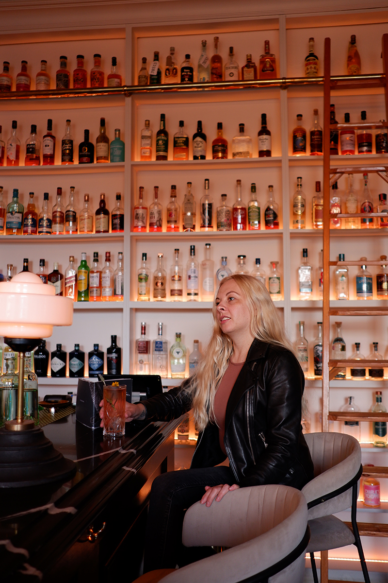 My favourite 8 bars and restaurants in Glasgow: Fly South a woman sitting by bar with a bottle shelf behind her 