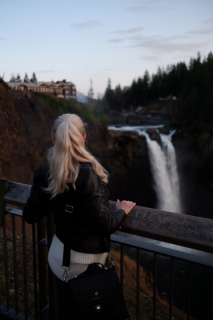 Snoqualmie falls and Salish lodge at the top, a woman is standing in the foreground, her back is to the camera